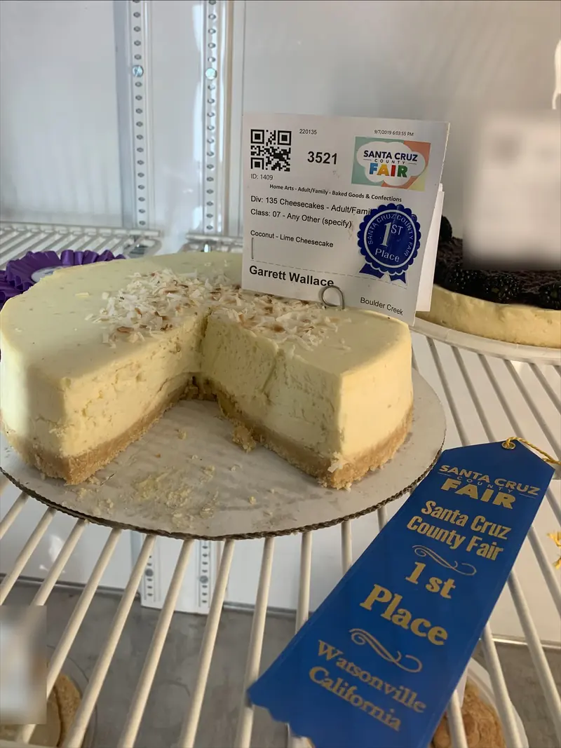 Garrett’s coconut-lime cheesecake in the fair’s display case, cut open, with his entry tag and a blue first-place ribbon