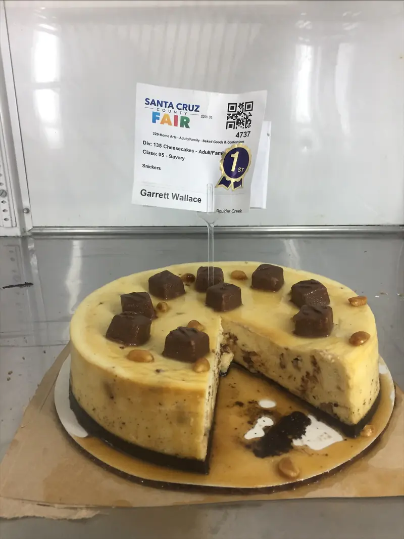 Garrett’s Snickers cheesecake with candy-bar pieces and peanuts on top, cut open, with a first-place sticker on its entry tag
